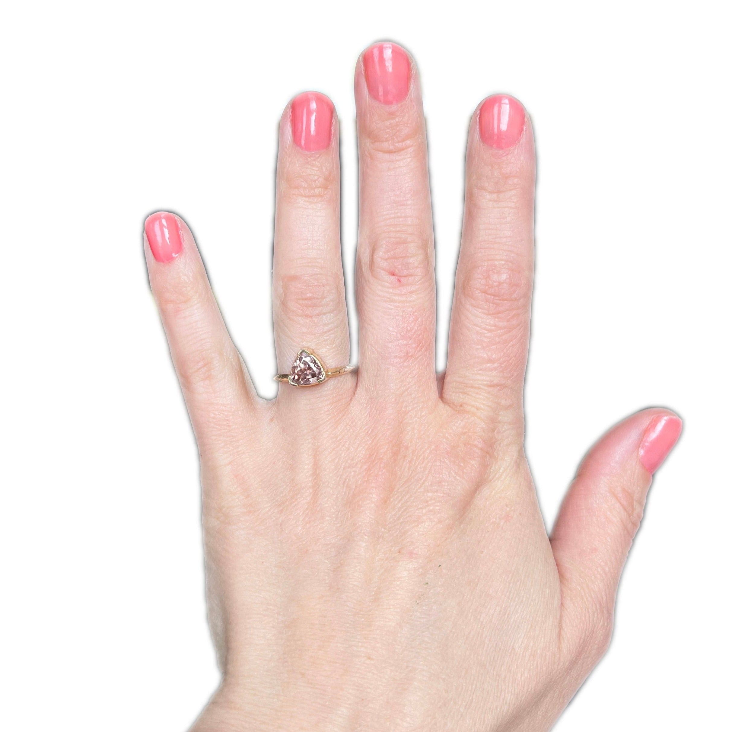Woman's finger adorned with the Umbra Trillion Ring, showcasing a rose-colored Australian zircon.